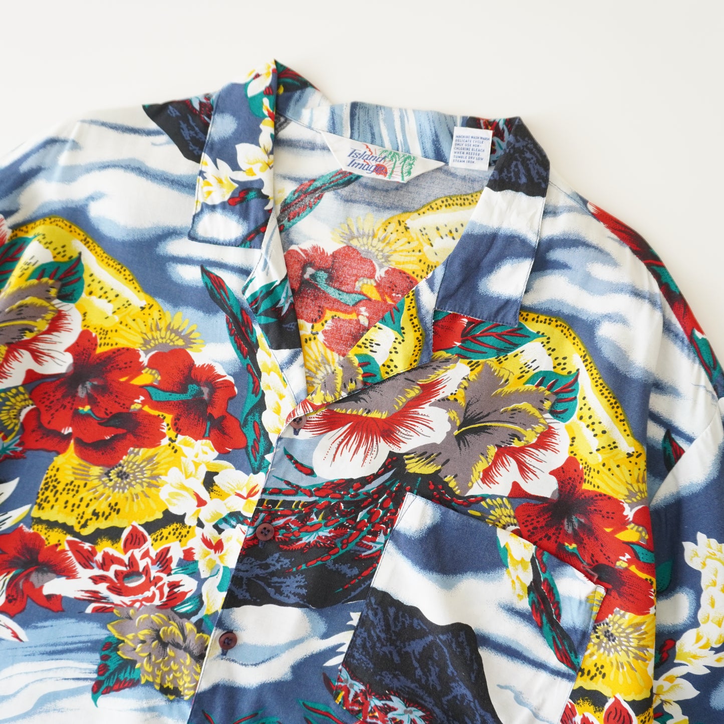 Thrifted - Camisa ISLAND Azul  y blanco, con flores /  Talla XL, 71 LARGO x 65 ANCHO.